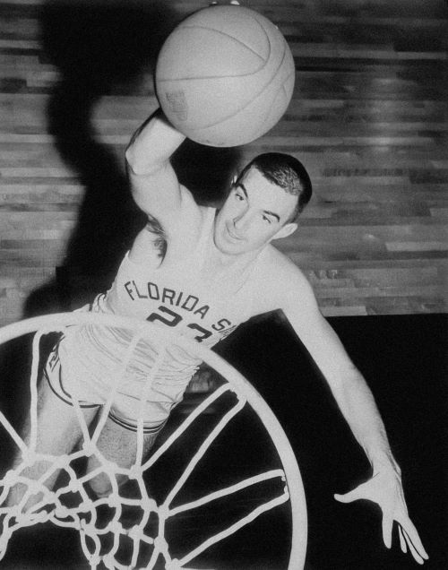 Basketball player wearing a Florida State jersey jumps to score through the hoop with one hand.