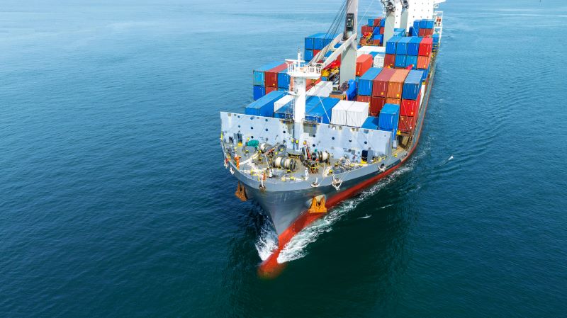 Cargo ship loaded with colorful shipping containers sailing on calm blue water.